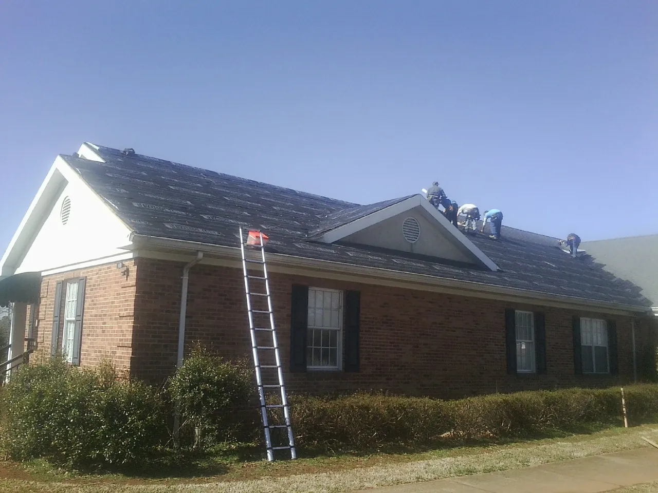 Crew tearing shingles off a brick ranch roof with a ladder set — Emergency Roof Repair work by our crew in Altamont