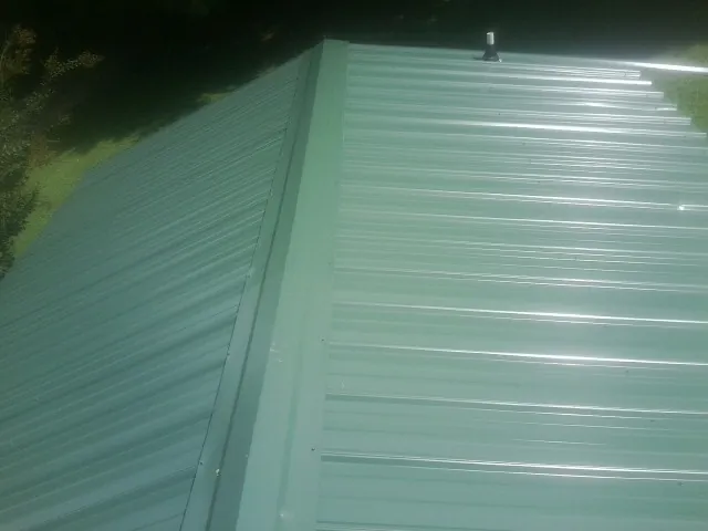 New green metal panels meeting at the ridge of a roof — Flat Roof Repair work by our crew in Altamont