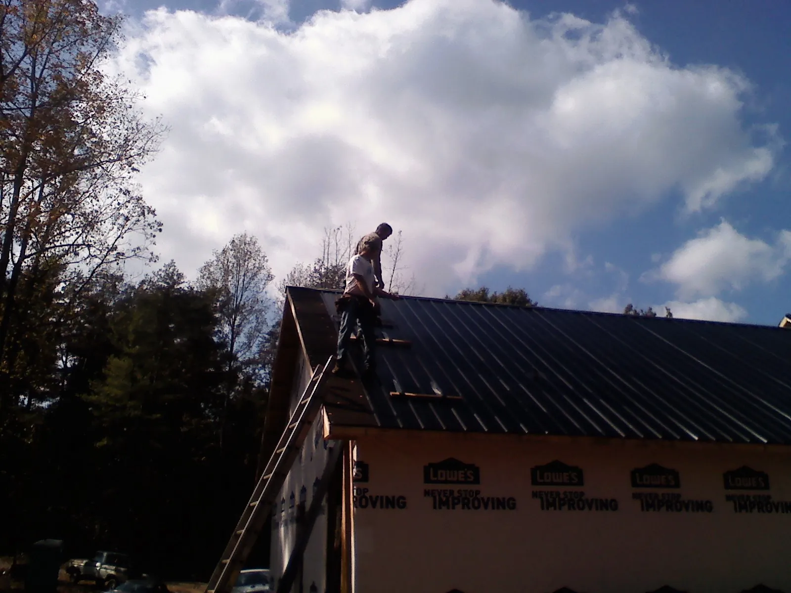 Roofer fastening dark metal panels high against a cloudy sky, from a Roof Inspection job in Altamont