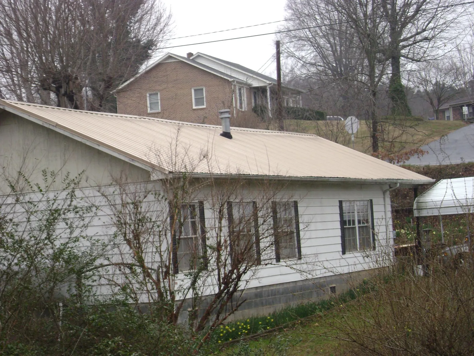 Tan metal roof on a white sided house set into a hillside — Commercial Roofing by Roofing Brothers in Altamont