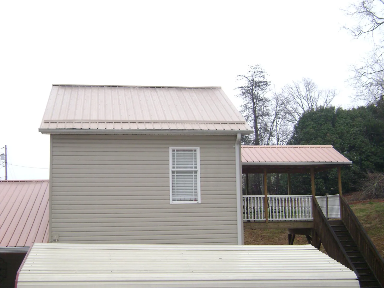 Tan metal roofs on a two story addition and attached porch, from a Roof Replacement job in Altamont